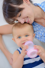 Mother cuddling baby chewing bottle
