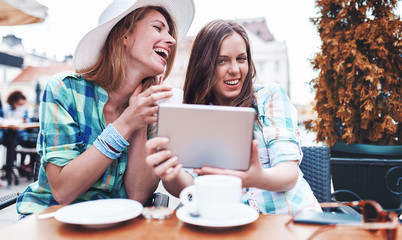Friends meeting in a cafe. Young women drinking coffee and have fun with tablet. Consumerism, lifestyle concept