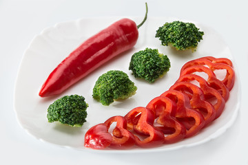 Slices of bell pepper, chili, broccoli on a white plate on a white background