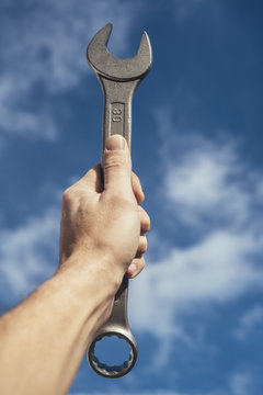 Big spanner wrench in the hand in front of the sky
