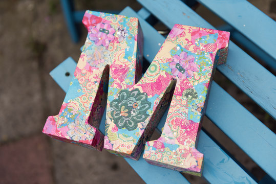 A very beautiful wooden 3d letter M on a blue wooden chair. A letter from the alphabet, the letter M