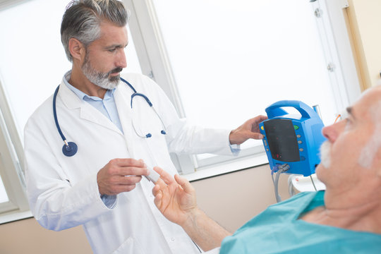 male doctor using lancelet on man at desk in clinic