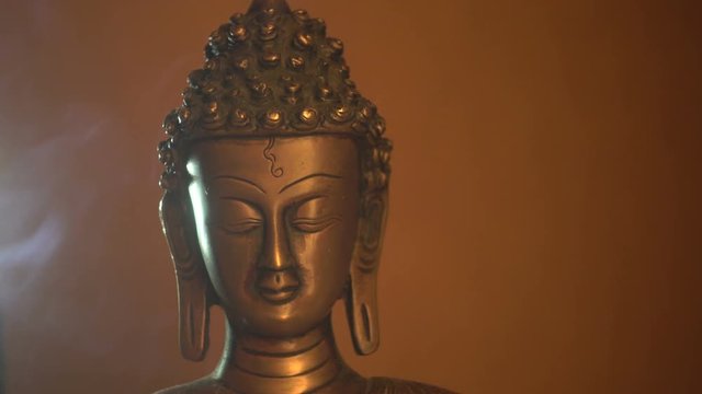 Copper statuette of Buddha,  Buddha's face close-up and smoke of incense sticks