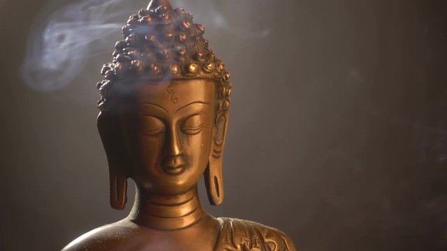 Rotation if statuette of Buddha and smoke of incense sticks