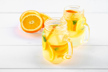 Orange detox water in mason jars on a white wooden table. Healthy food, drinks.