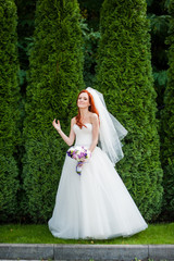 Obraz na płótnie Canvas Beautiful smiling red hair bride with wedding bouquet