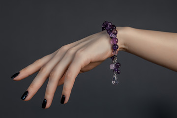 женская кисть руки с черным лаком на ногтях и красивым браслетом из сиреневых драгоценных камней 
