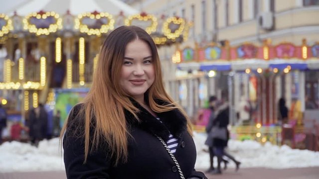 Smiling fat woman looks in camera and stands at the carousel background