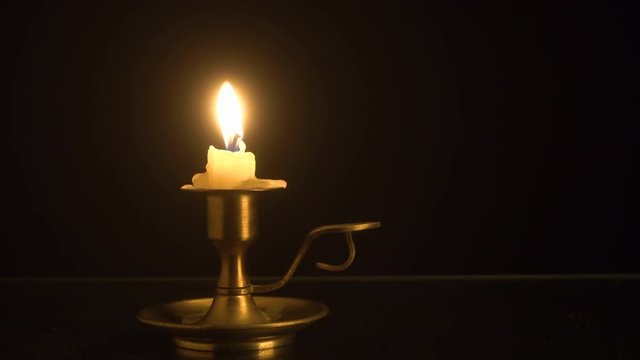 Burning candle on the old brass candlestick over black background