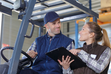 workers in logistics warehouse at forklift checking list