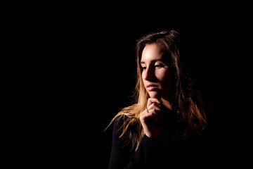 Brown-haired girl in black holds her hand under her chin and looks down thoughtfully with a place...