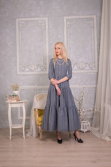 Blonde girl in a long grey dress standing in grey vintage interiors