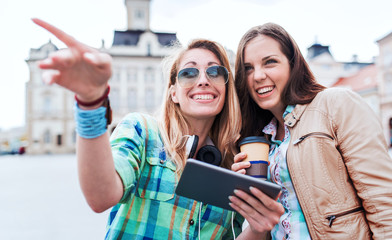 Young smiling girls enjoying in the city, having fun with tablet. Lifestyle, technology