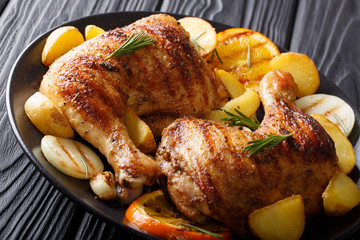 Homemade BBQ: Grilled chicken legs with orange, lemon, onions, garlic and potatoes Close-up on a plate. horizontal