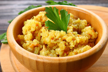 Rice pilaf with chicken, spices and parsley in a bowl on a wooden table.