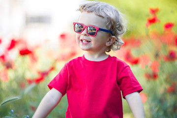 Pretty blond boy is wearing sunglasses holding red poppy flower
