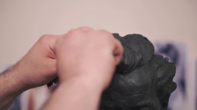 A sculptor who works on his clay sculpture in his workshop. Clip. Man cuts a mold of clay