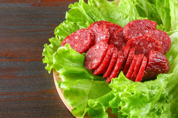 Smoked sausage, salami chopped in slices on a salad on a wooden circular cutting board on a brown table.