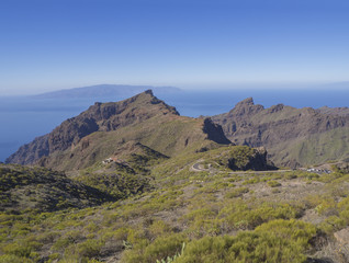 view on asfalt road to village Masca with green hills, sharp mountain peaks, sea horizon and clear blue sky background