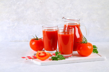 Tomato juice in glasses and a pitcher on a gray concrete table.
