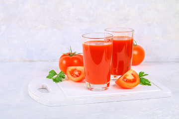 Tomato juice in glasses on a gray concrete table.