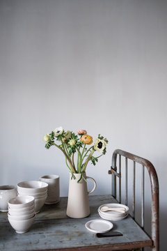Flowers vase with crockery on shelf against white wall