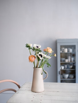 Vase mit Ranunkeln und Anemonen auf Küchentisch in Steinkrug