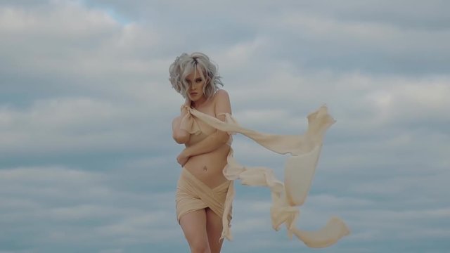 Mythical image of beautiful woman walking in background of cloudy sky. Goddess descended from heaven to earth, approaching and seductivly looking in camera