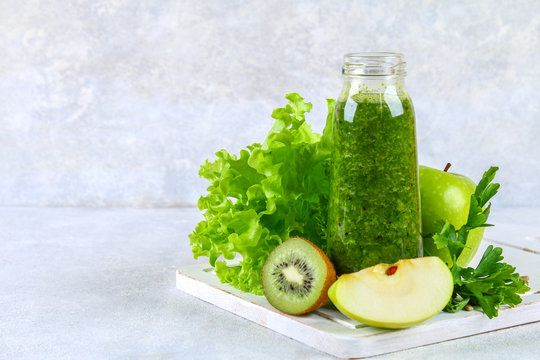 Green smoothies from parsley, salad, kiwi, apple in a bottle on a gray concrete table.