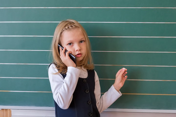 A first grade student at school speaks by phone. emotions of schoolgirls