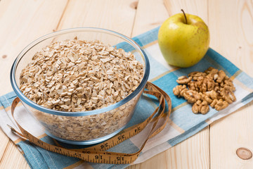 oat flakes in a glass plate, nuts and apples on a wooden board, concept of a healthy lifestyle