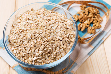 oat flakes in a glass plate, nuts and apples on a wooden board, concept of a healthy lifestyle