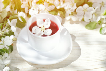 Obraz na płótnie Canvas Mug of tea and blossom on a white wooden background. Sunny day