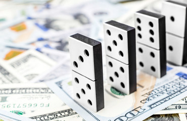 Row of domino pieces which stay on background of dollar bills.