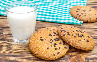 Glass of milk, cookies with chocolate and kitchen towel on the table.