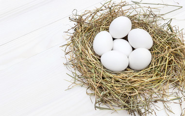Nest with eggs on white wooden table.