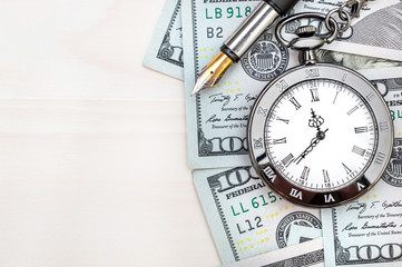 Pocket watch with dollar bills and pen on white wooden background. Business background.