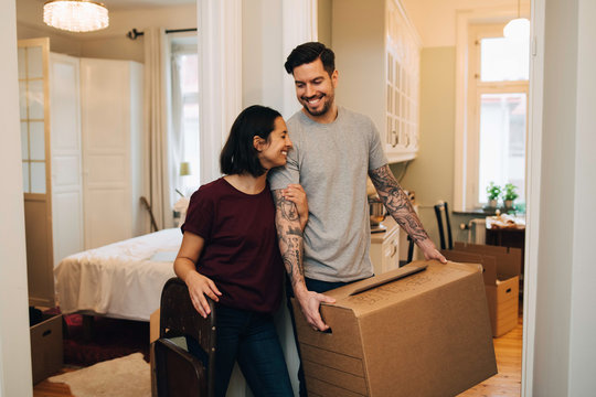 Cheerful woman standing with man carrying box at home - Powered by Adobe