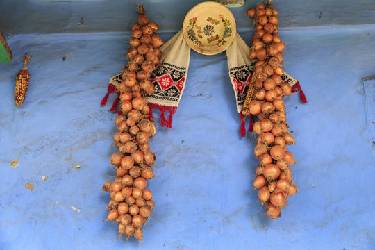 Europe, Romania. Onions drying on side of house next to pottery and embroidery.