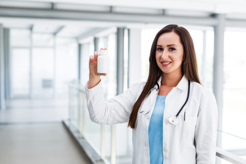 Young female doctor smiles and holds blank bottle