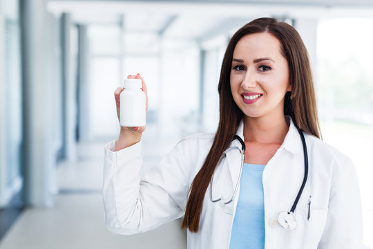 Young female doctor smiles and holds blank bottle