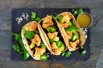 Roasted coconut cauliflower tacos. Healthy, vegan meal. Above view on a dark slate stone background.