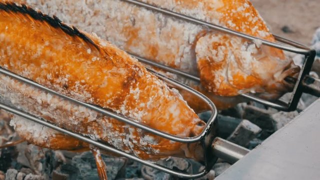 National Thai dish, fried fish on spit in salt and with greens close up view. Exotic food of Thailand and Asia