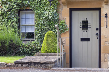 Grey wooden doors with a small window in an old traditional English stone cottage, surrounded by...