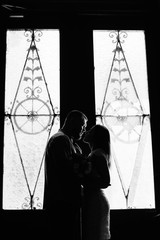 portrait of a romantic couple in a backlight from a window or door, silhouette of a couple in a doorway with a backlight, couple of lovers groom and bride at the window, black and white photography