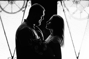 portrait of a romantic couple in a backlight from a window or door, silhouette of a couple in a doorway with a backlight, couple of lovers groom and bride at the window, black and white photography