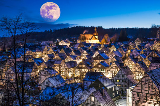 Full moon rising above a tiny snow covered timber framed, myth village.
