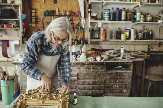 Woman restoring gilded frame in workshop