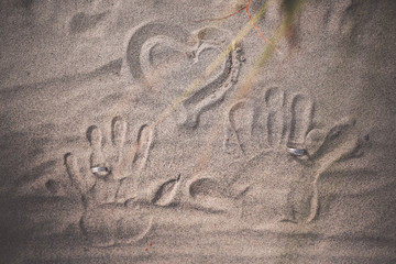 Hands prints on the sand with wedding rings. Heart drawn in the beach. Love and wedding concept. 