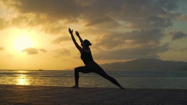 Silhouette girl do warrior I yoga pose at sunset beach rapid slow motion